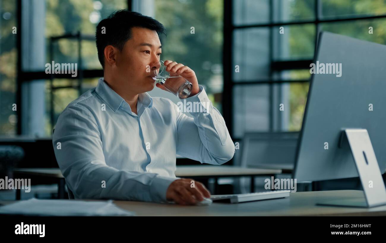 Homme coréen asiatique boire un verre d'eau fraîche maintenir l'équilibre santé rajeunissement énergie soins de santé habitude homme d'affaires assis au bureau sur ordinateur Banque D'Images