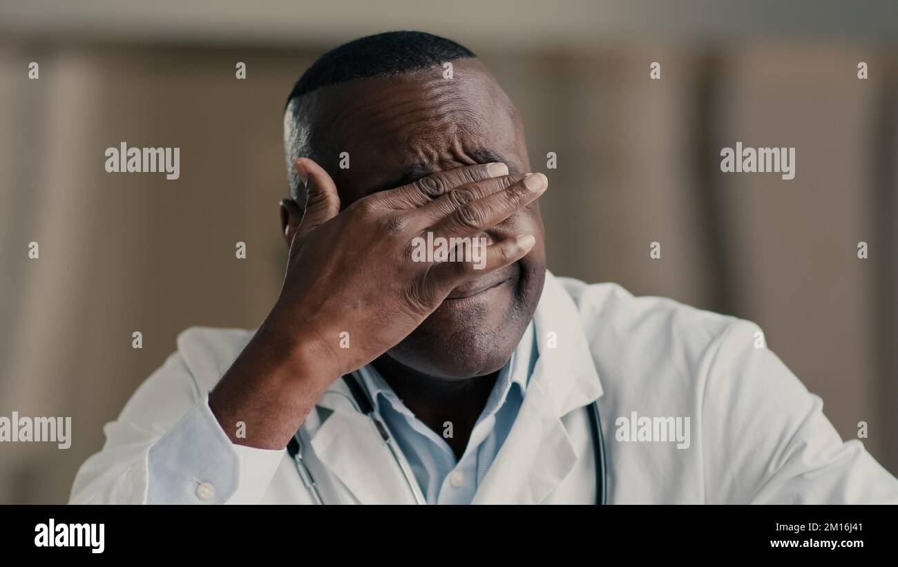 Homme africain fatigué médecin médecin praticien travailleur médical frotter yeux irrités massage visage homme ethnique thérapeute épuisé après la journée de travail Banque D'Images