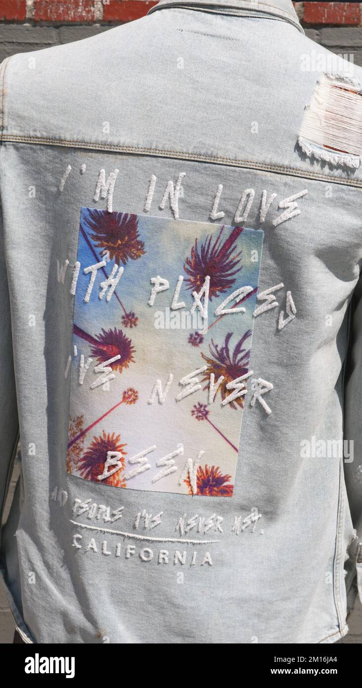 « Je suis amoureux des endroits que je n'ai jamais vus et des gens que je n'ai jamais rencontrés » écrit au dos d'une veste en Jean denim sur un imprimé palmiers Banque D'Images