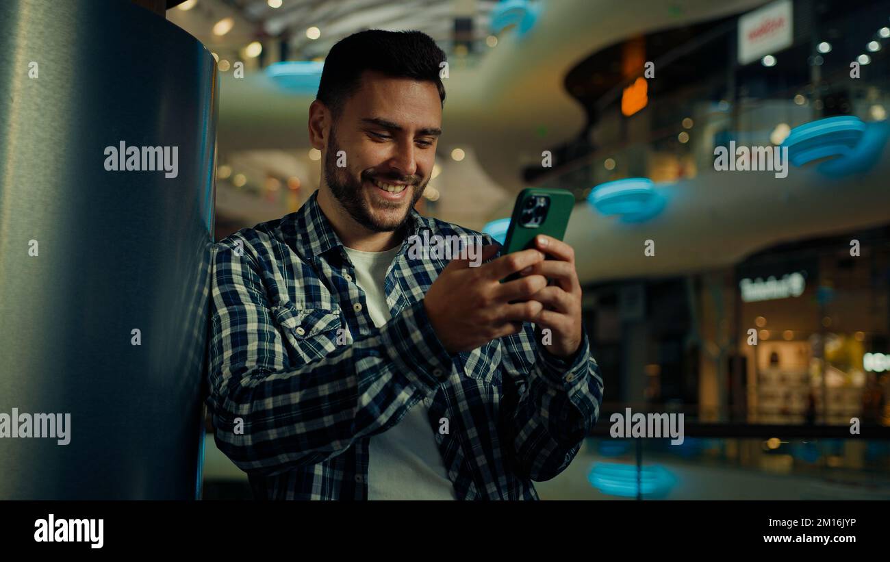 Jeune homme blogueur arabian hispanic homme d'affaires stand dans le centre commercial regarder l'écran mobile SMS message e-mail lire les nouvelles positives sur le téléphone portable Banque D'Images