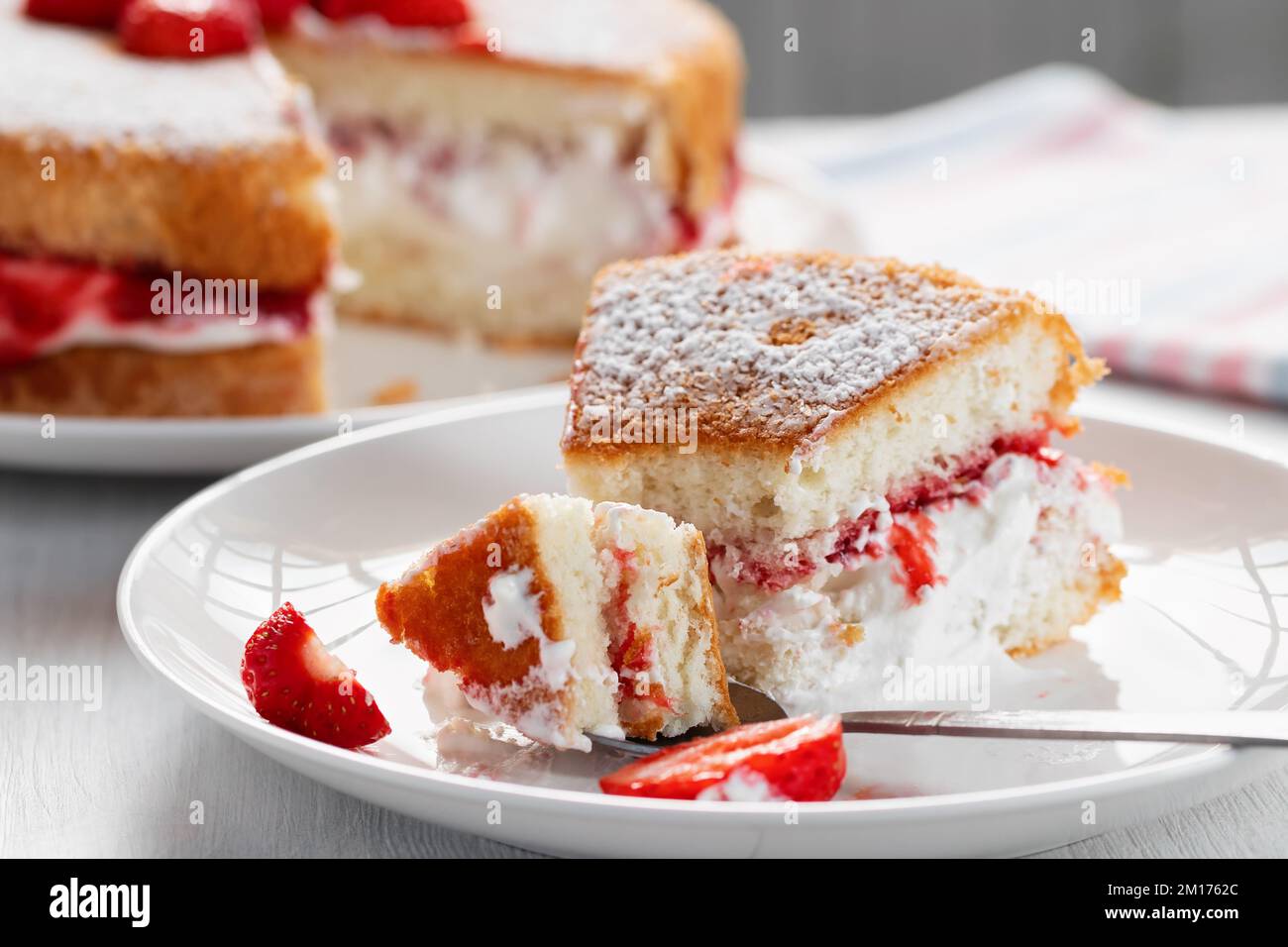 Manger un morceau de gâteau Victoria avec de la crème fouettée, de la confiture et des fraises fraîches. Banque D'Images