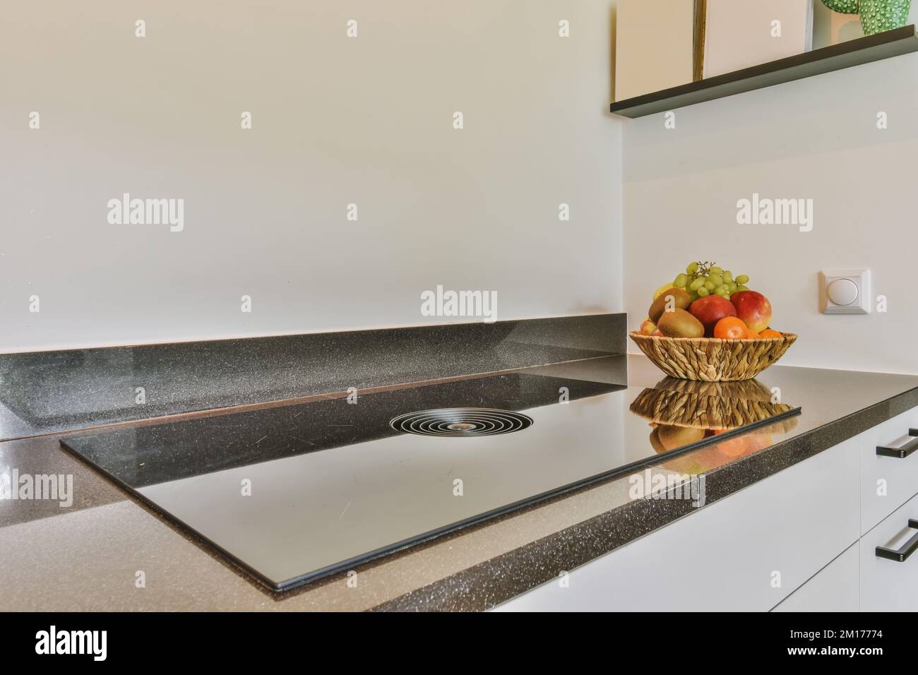un bol de fruits assis sur le comptoir de la cuisine devant un évier qui est blanc et a le granit noir Banque D'Images