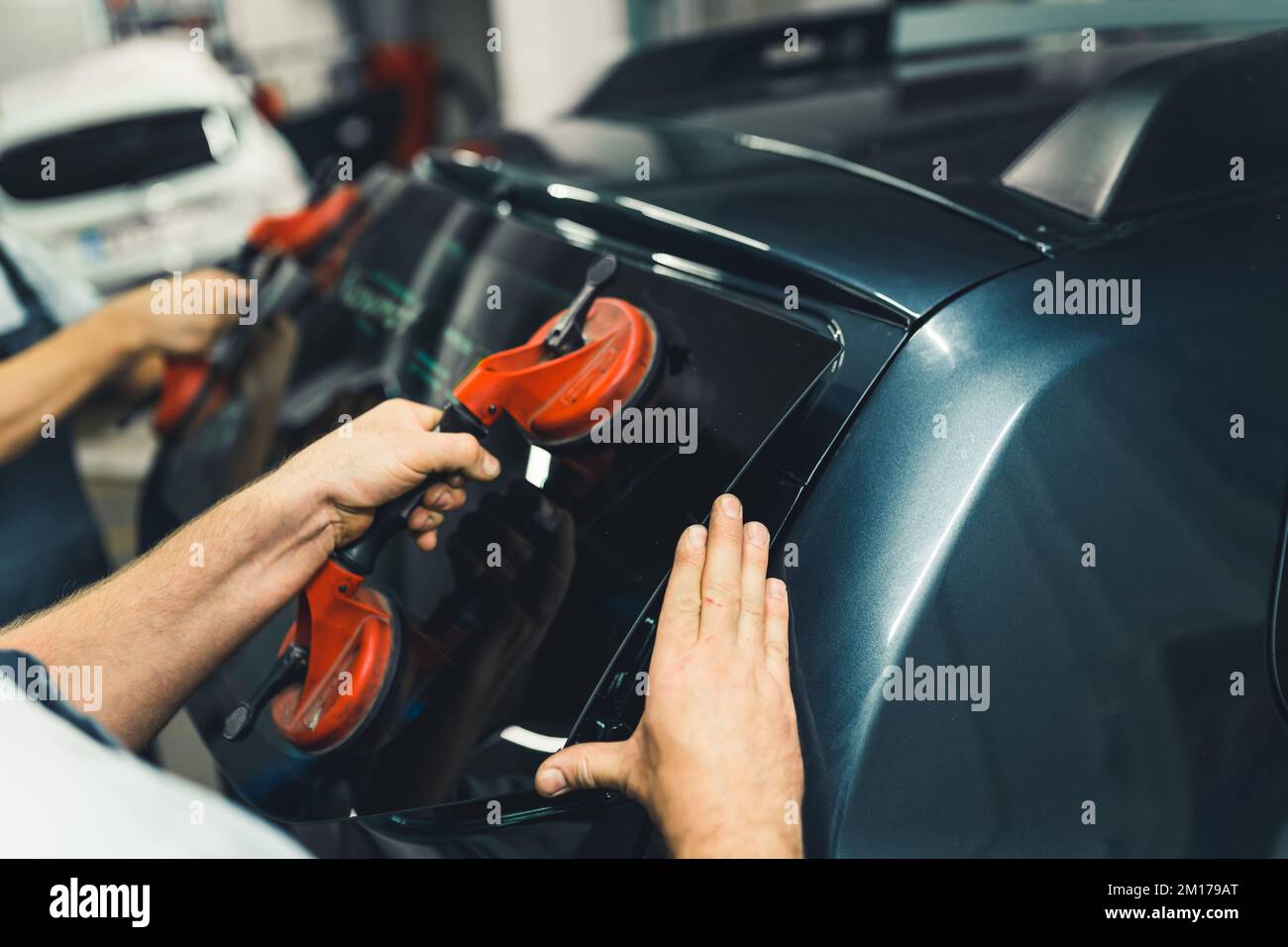 Les ventouses de glace sont nécessaires dans le kit de réparation de pare-brise et de lunette arrière. Mains de deux mécaniciens caucasiens non reconnaissables qui retirent la lunette arrière de la voiture noire. Photo de haute qualité Banque D'Images
