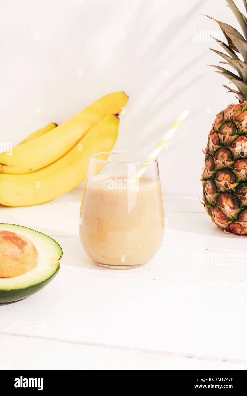 Smoothie à la banane, à l'ananas et à l'avocat sur une table en bois blanc au soleil. Concept minimal de diète de détox, boisson de vitamine d'été. Banque D'Images