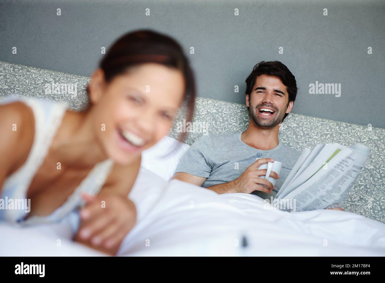 Détendu et heureux. Photo d'un homme au lit souriant à sa petite amie avec un journal et une tasse dans la main. Banque D'Images