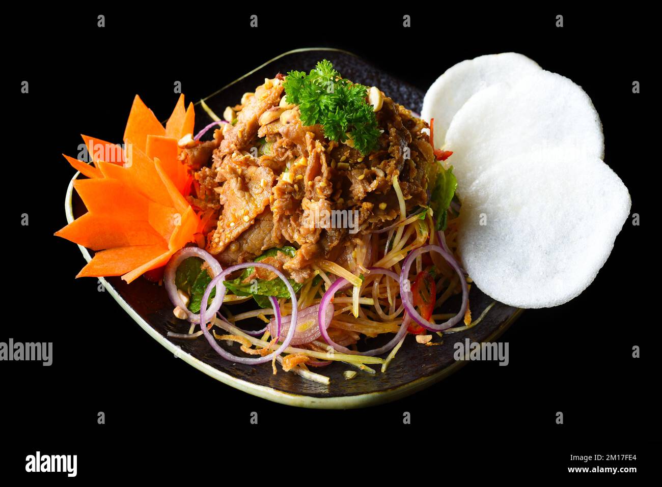 Salade de bœuf asiatique avec papaye verte servie avec des chips de riz isolées sur fond noir vue latérale Banque D'Images