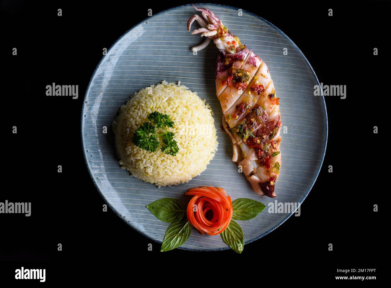 Calmar grillé avec riz blanc sur une plaque bleue isolée sur fond noir vue du dessus Banque D'Images