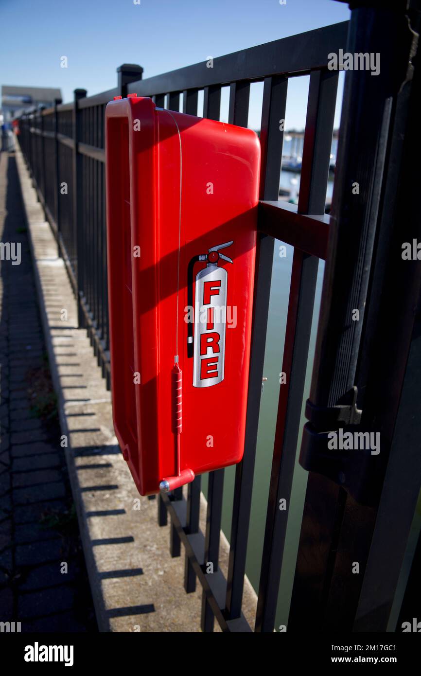 Une boîte rouge avec un petit marteau suspendu à proximité et attaché à une clôture en métal à la marina de la ville, près des quais Banque D'Images