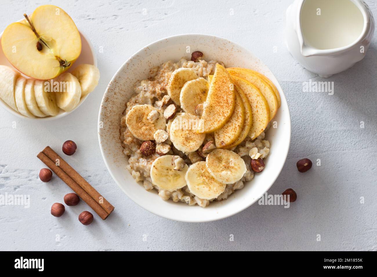 Délicieux petit déjeuner sain. Flocons d'avoine avec banane, pomme, noix et cannelle sur fond gris clair, vue du dessus Banque D'Images