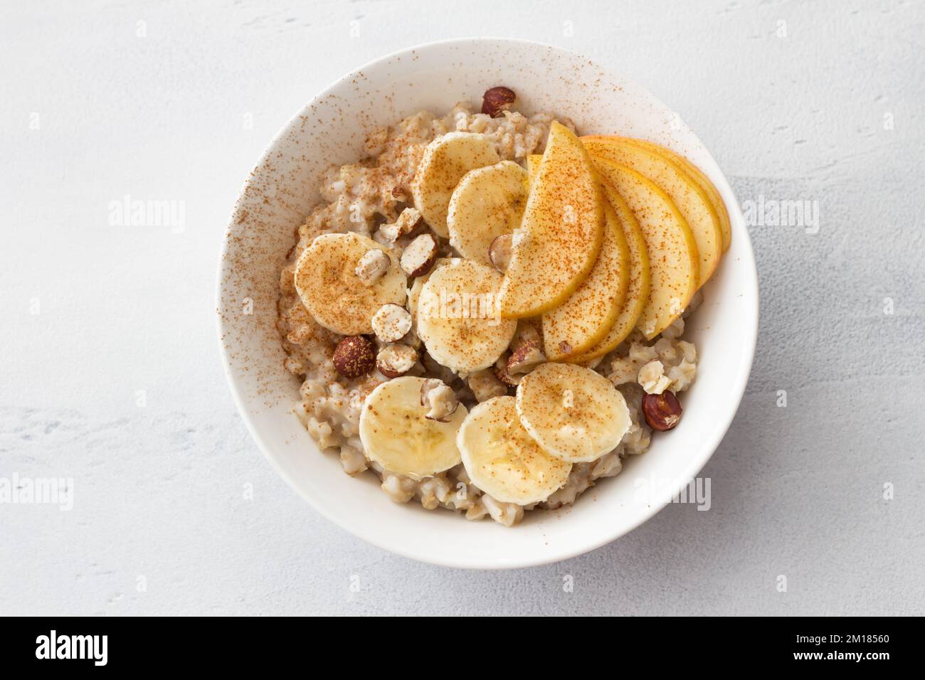 Délicieux petit déjeuner sain. Flocons d'avoine avec banane, pomme, noix et cannelle sur fond gris clair, vue du dessus Banque D'Images