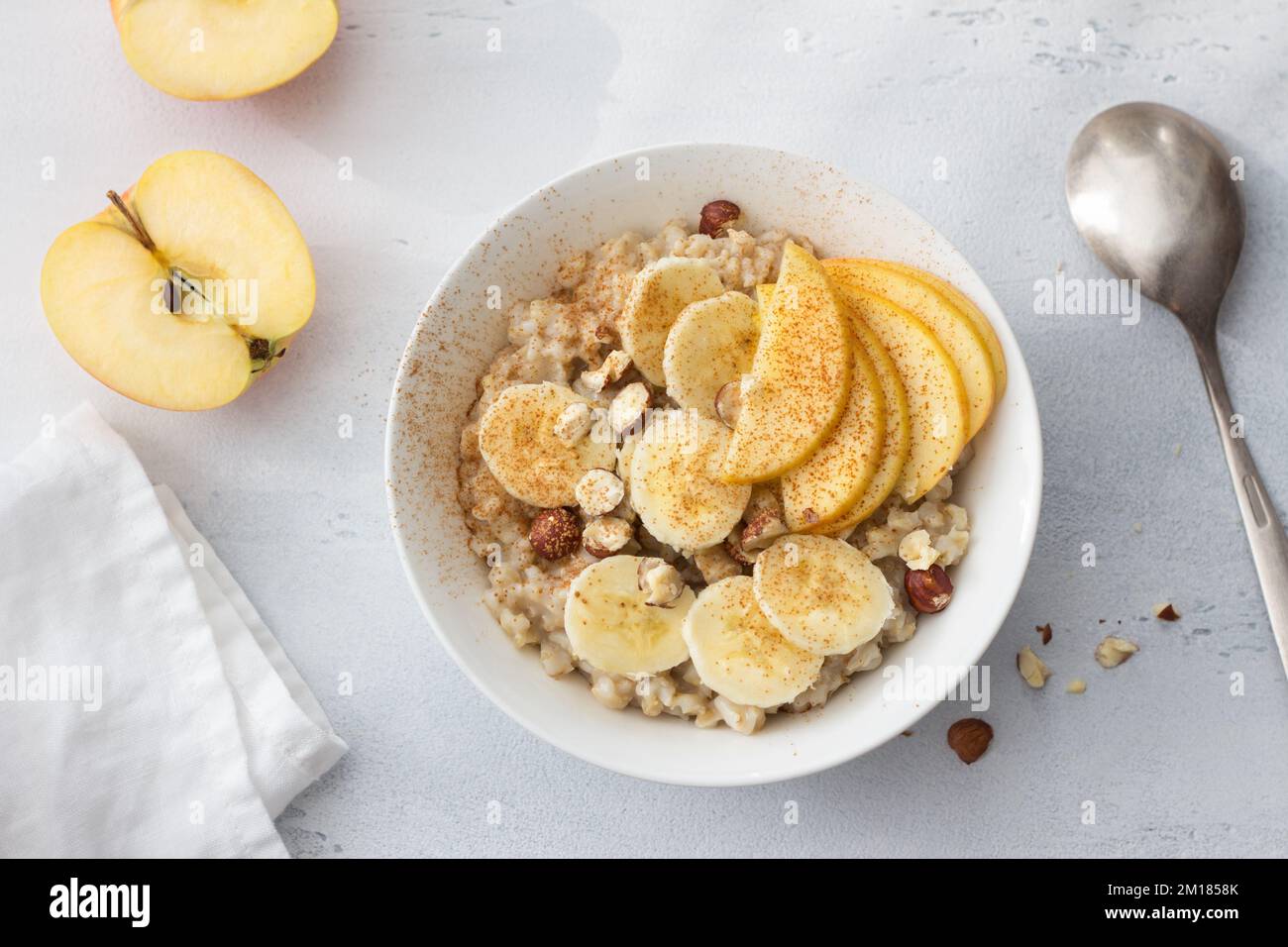 Délicieux petit déjeuner sain. Flocons d'avoine avec banane, pomme, noix et cannelle sur fond gris clair, vue du dessus Banque D'Images