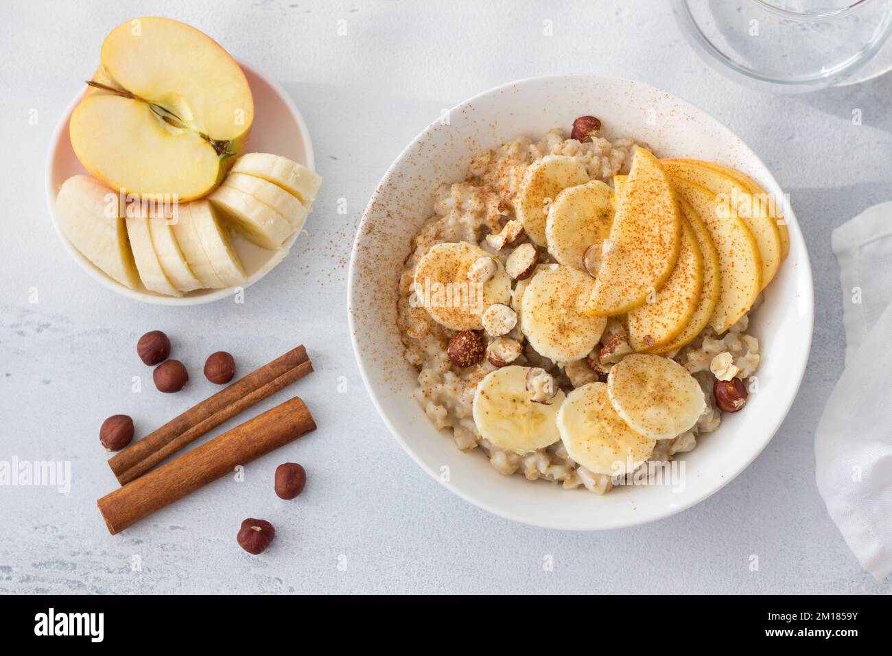 Délicieux petit déjeuner sain. Flocons d'avoine avec banane, pomme, noix et cannelle sur fond gris clair, vue du dessus Banque D'Images