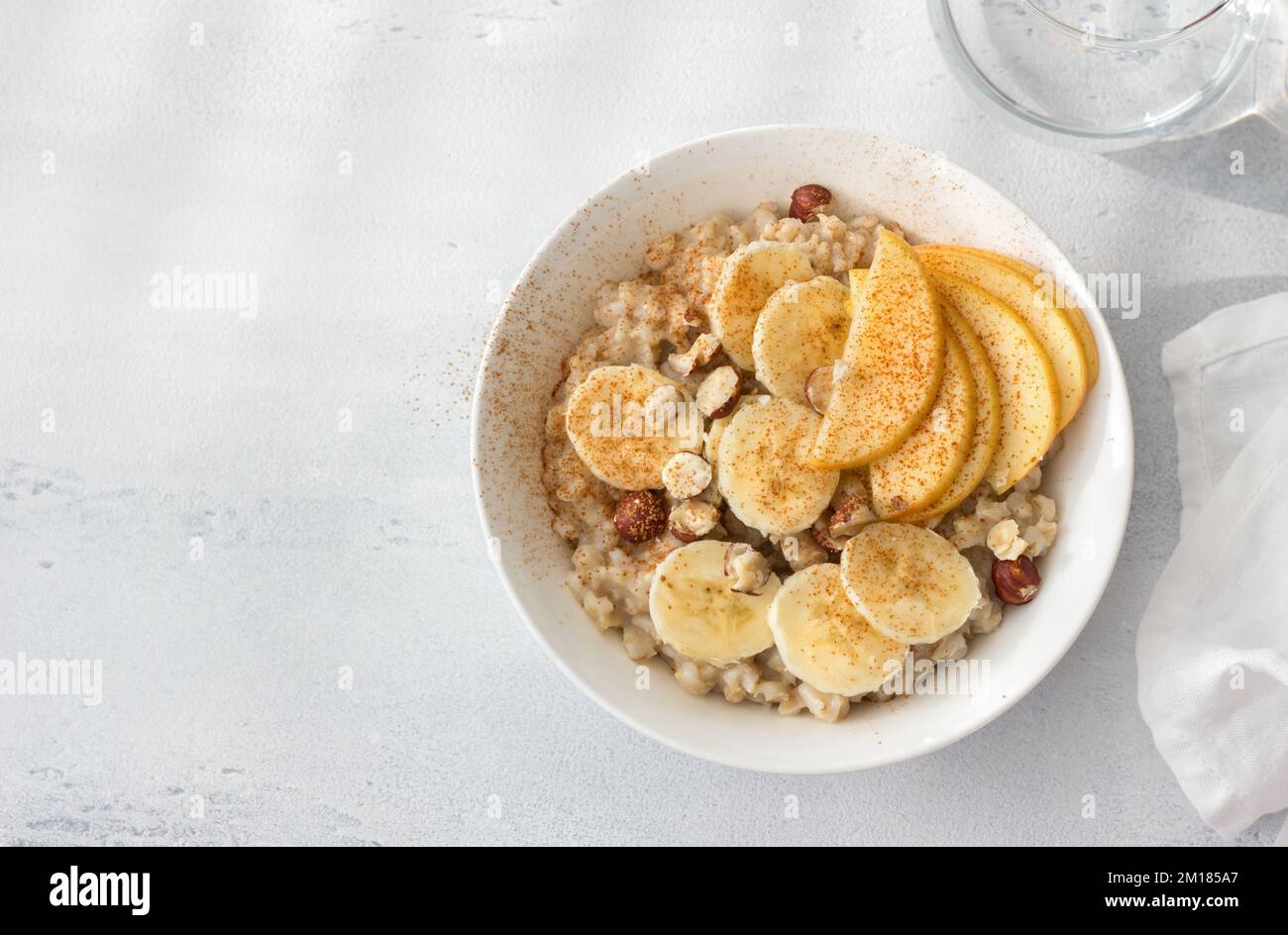 Délicieux petit déjeuner sain. Flocons d'avoine avec banane, pomme, noix et cannelle sur fond gris clair, vue du dessus, espace Banque D'Images