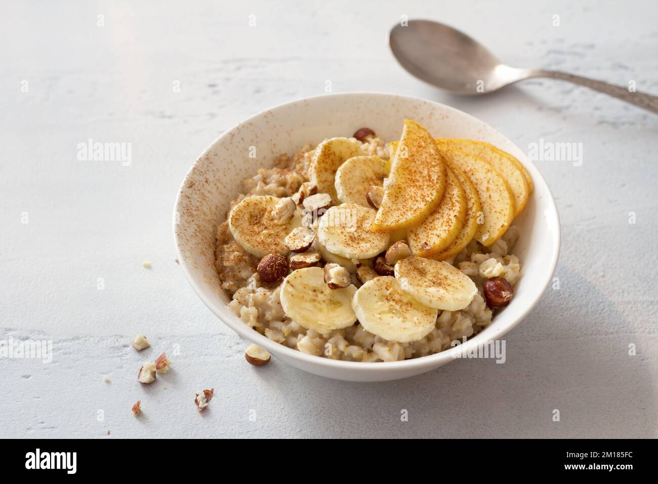 Délicieux petit déjeuner sain. Flocons d'avoine avec banane, pomme, noix et cannelle sur fond gris clair Banque D'Images