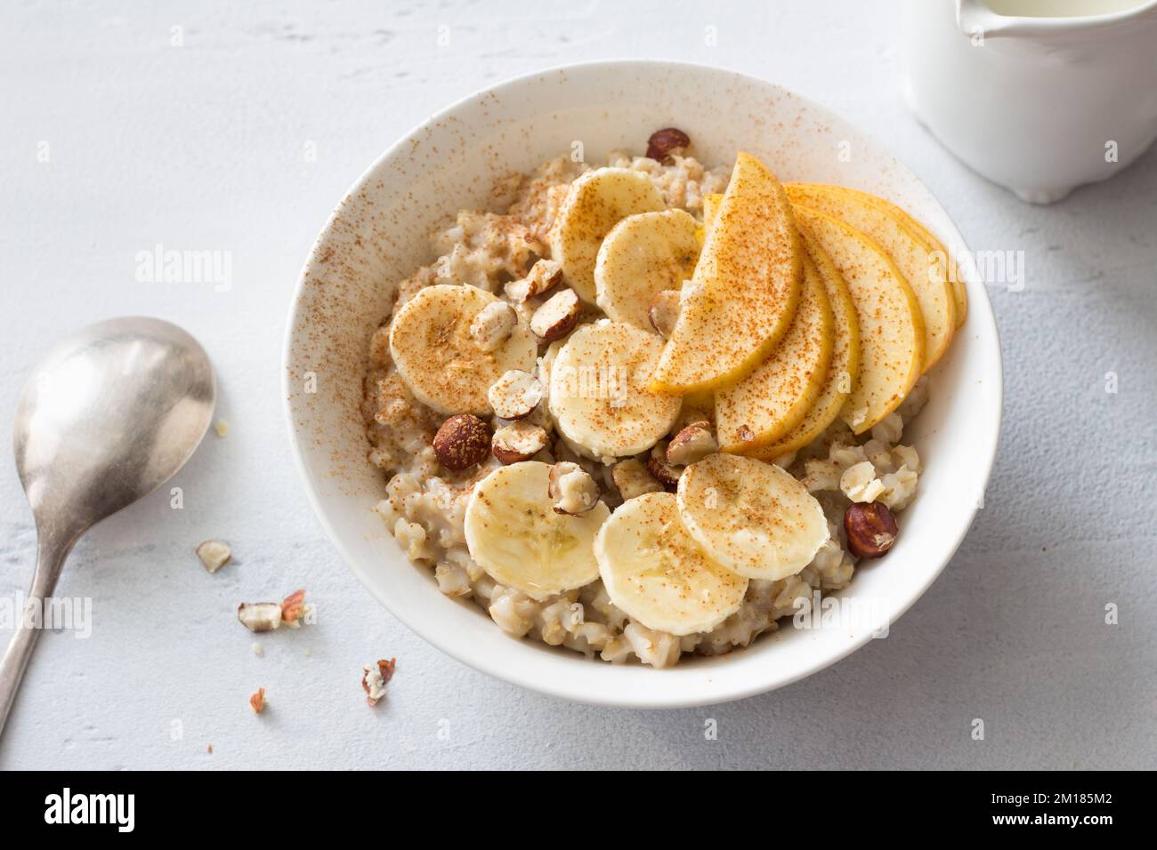 Délicieux petit déjeuner sain. Flocons d'avoine avec banane, pomme, noix et cannelle sur fond gris clair, vue du dessus Banque D'Images