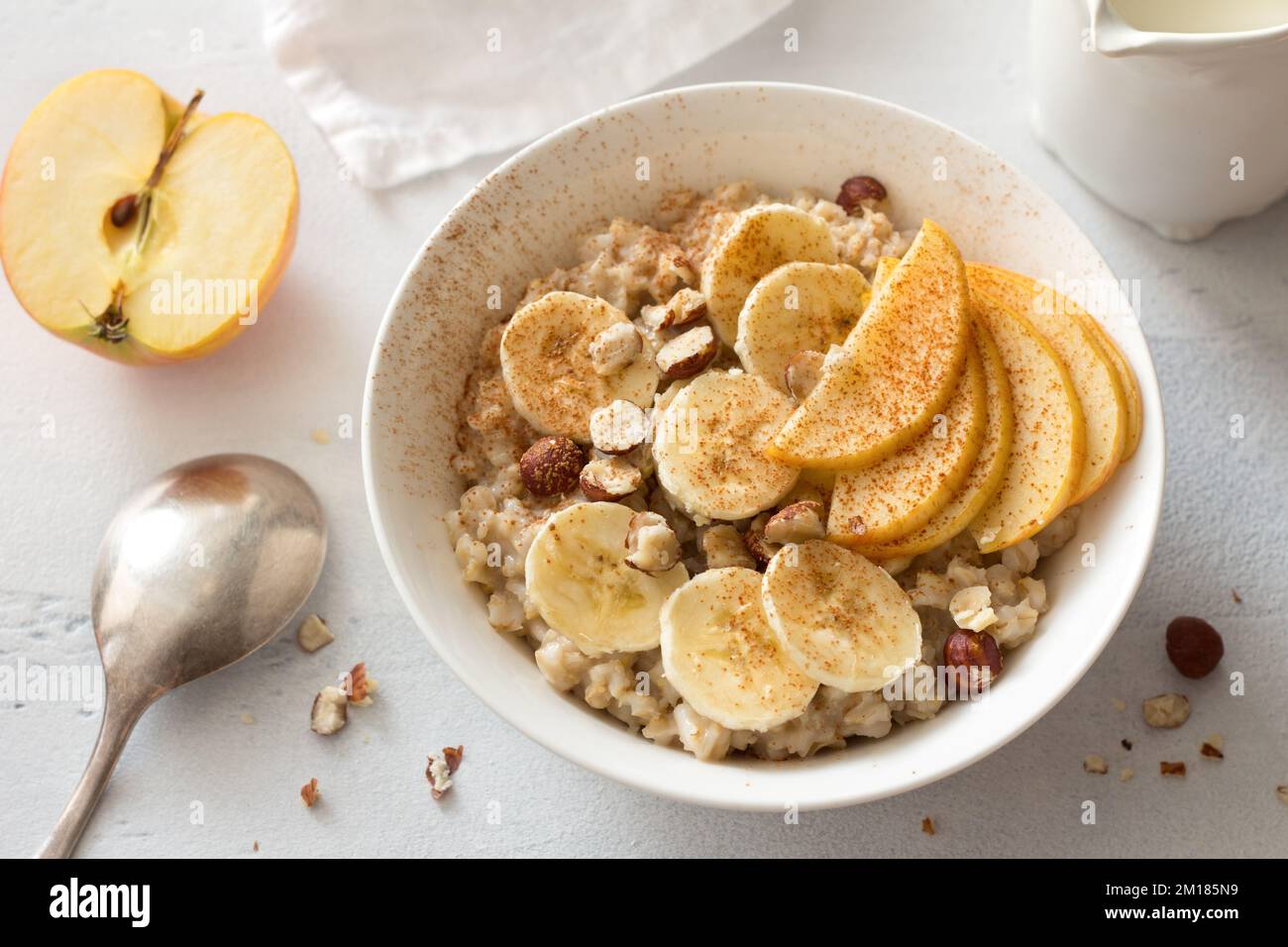 Délicieux petit déjeuner sain. Flocons d'avoine avec banane, pomme, noix et cannelle sur fond gris clair, vue du dessus Banque D'Images