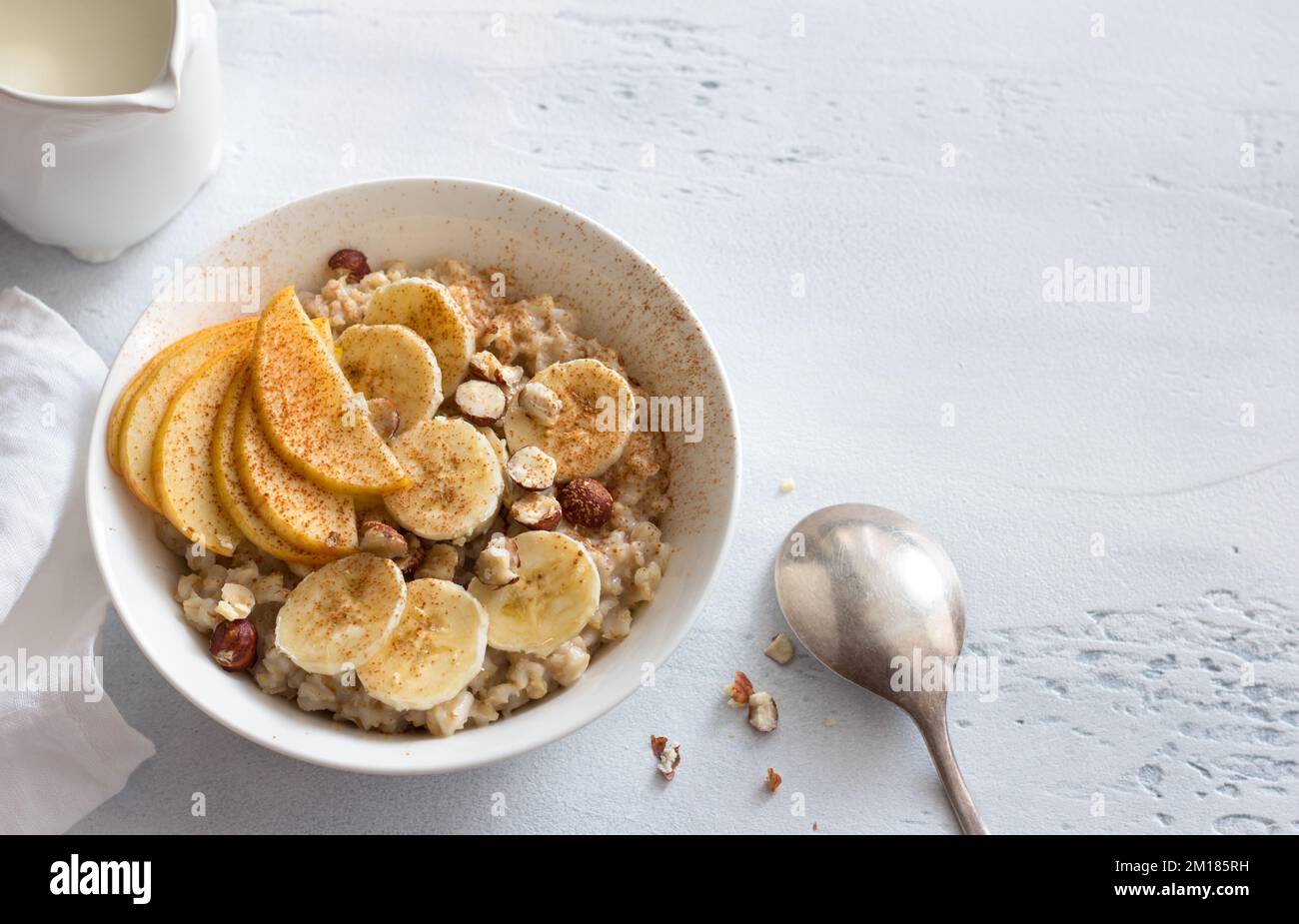 Délicieux petit déjeuner sain. Flocons d'avoine avec banane, pomme, noix et cannelle sur fond gris clair, vue du dessus, espace Banque D'Images