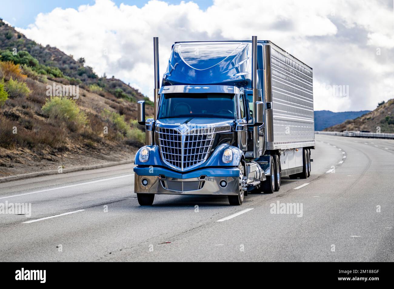 Tracteur semi-remorque bleu de grande taille de classe industrielle avec pièces chromées transportant des marchandises commerciales congelées dans un réfrigérateur semi-remorque en marche o Banque D'Images