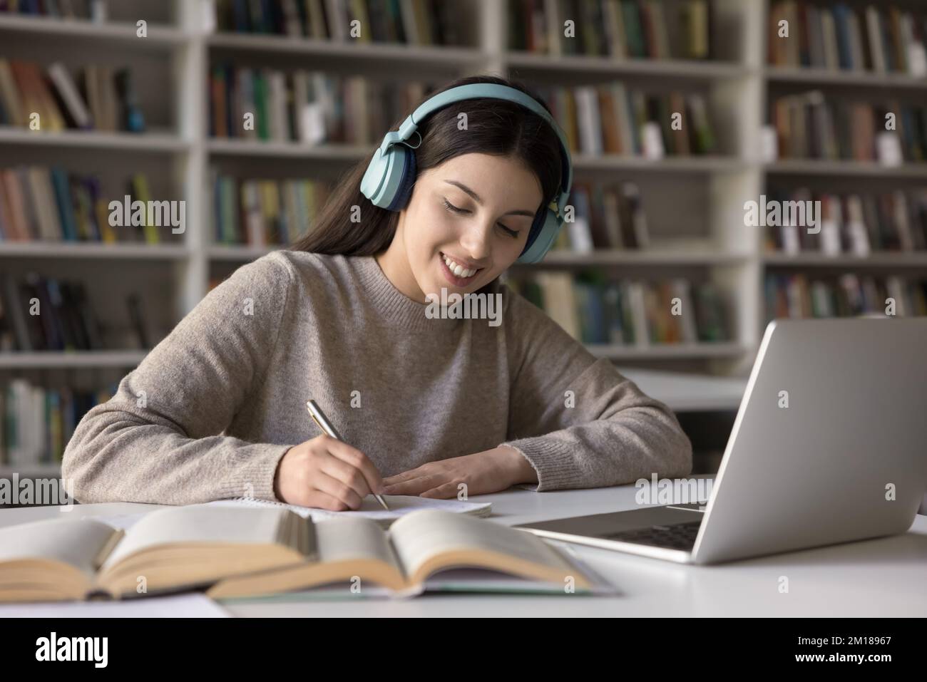 Bonne étudiante latine jeune fille dans des écouteurs sans fil étudiant dans la bibliothèque Banque D'Images