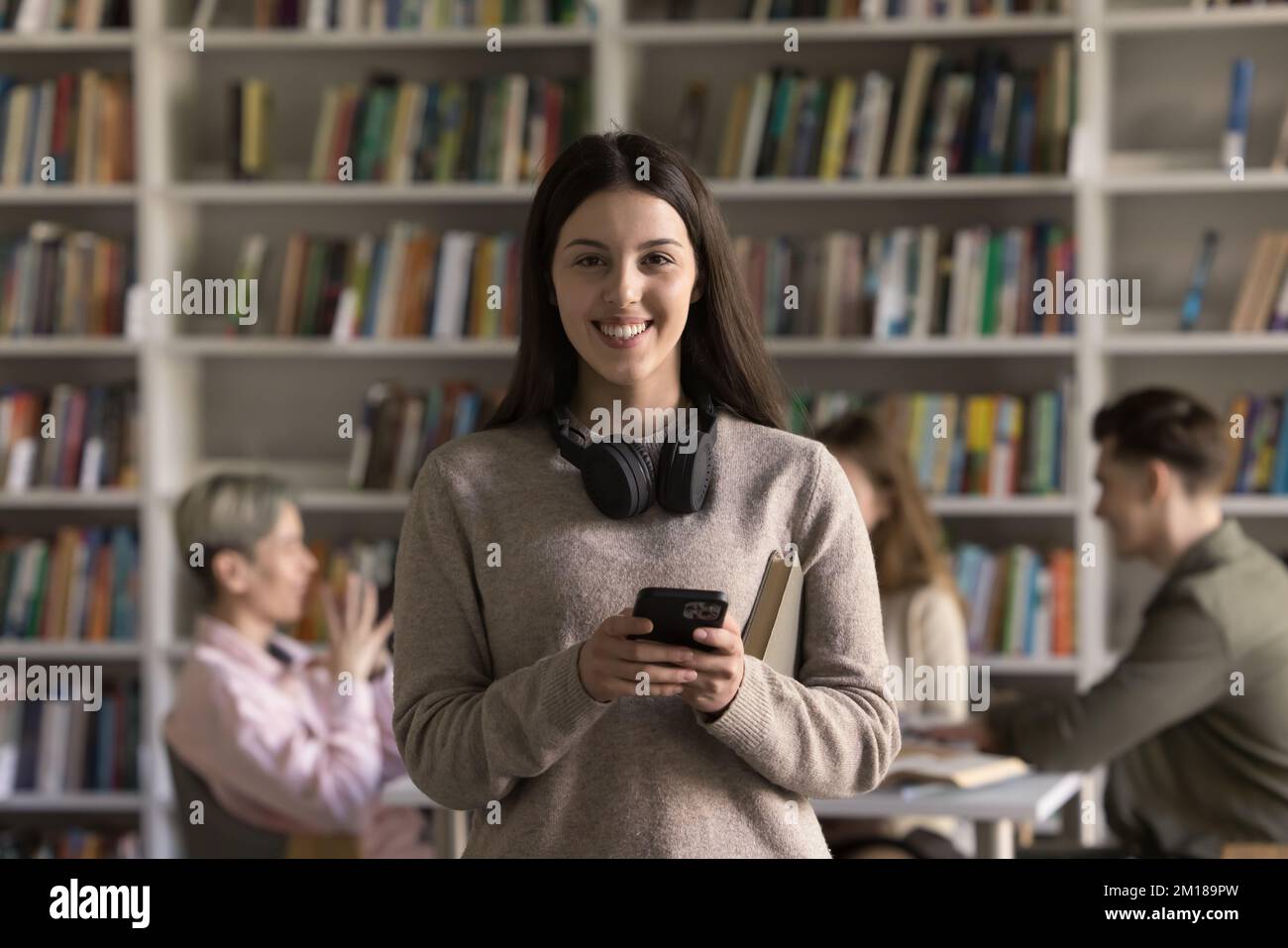 Bonne jolie fille étudiante latine tenant un téléphone portable, regardant l'appareil photo Banque D'Images