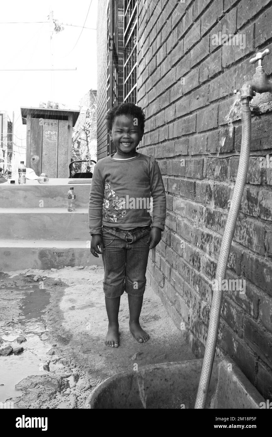 Une photo en niveaux de gris d'une petite fille africaine éclaboussé par l'eau d'un demi-tube Banque D'Images