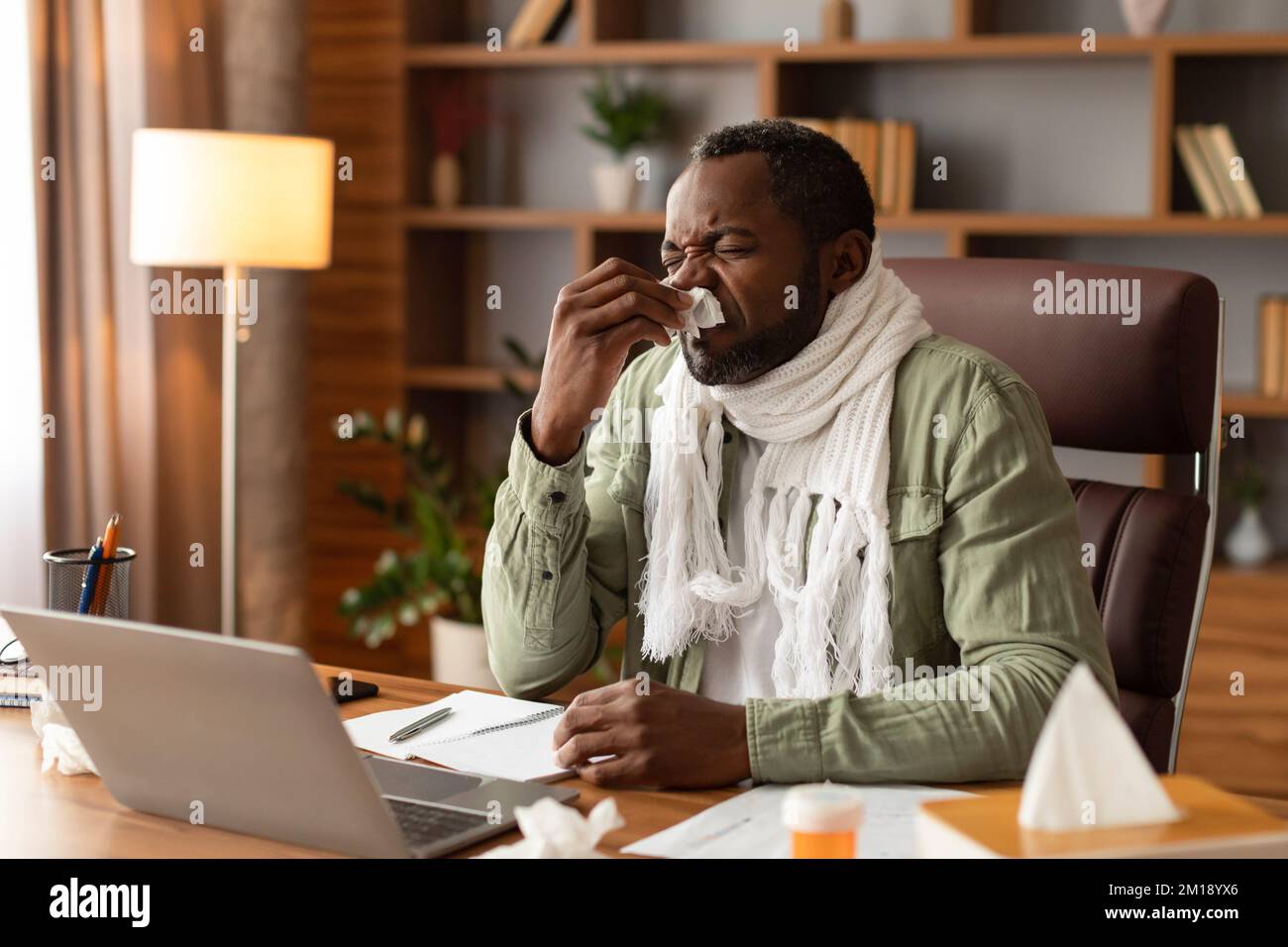 Malheureux triste adulte noir homme avec foulard souffle son nez dans la serviette, souffre de nez et de fièvre, travaille avec l'ordinateur Banque D'Images