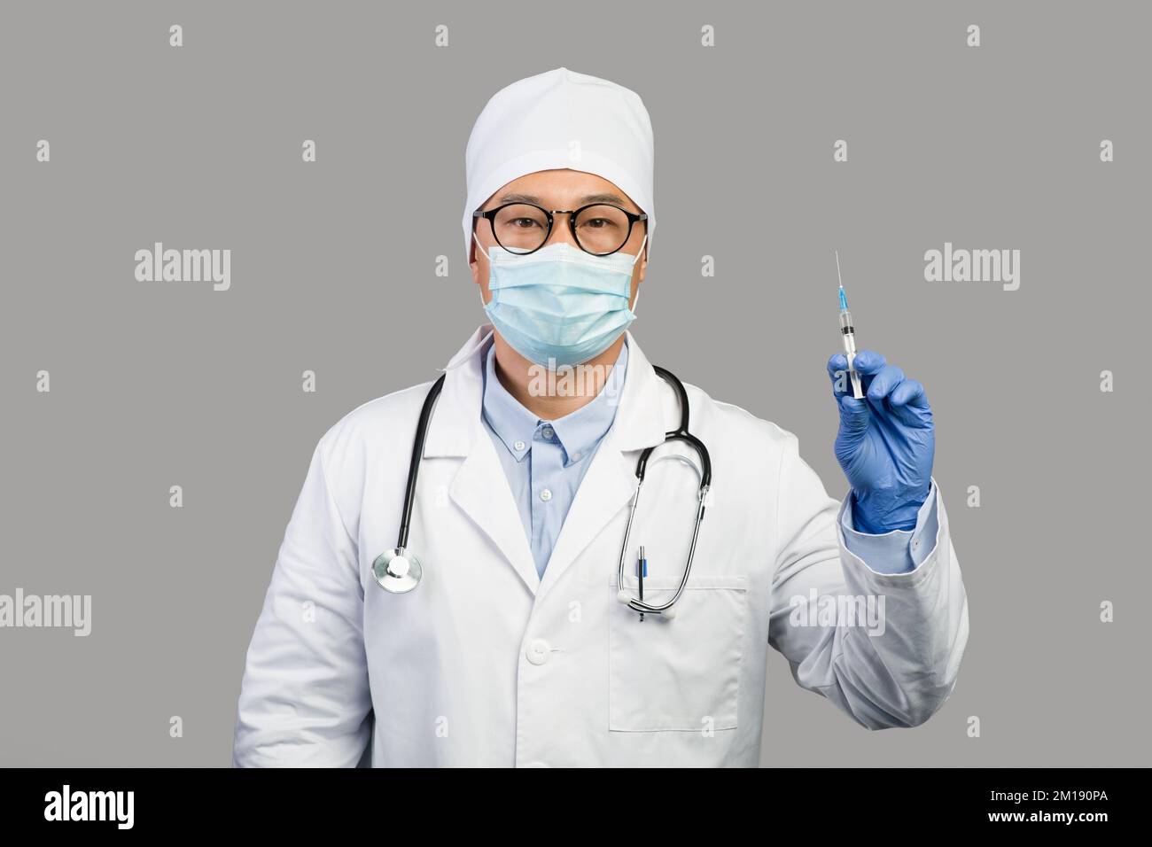 Homme chinois sérieux mature thérapeute en manteau blanc et masque de protection montre la seringue avec le vaccin Banque D'Images