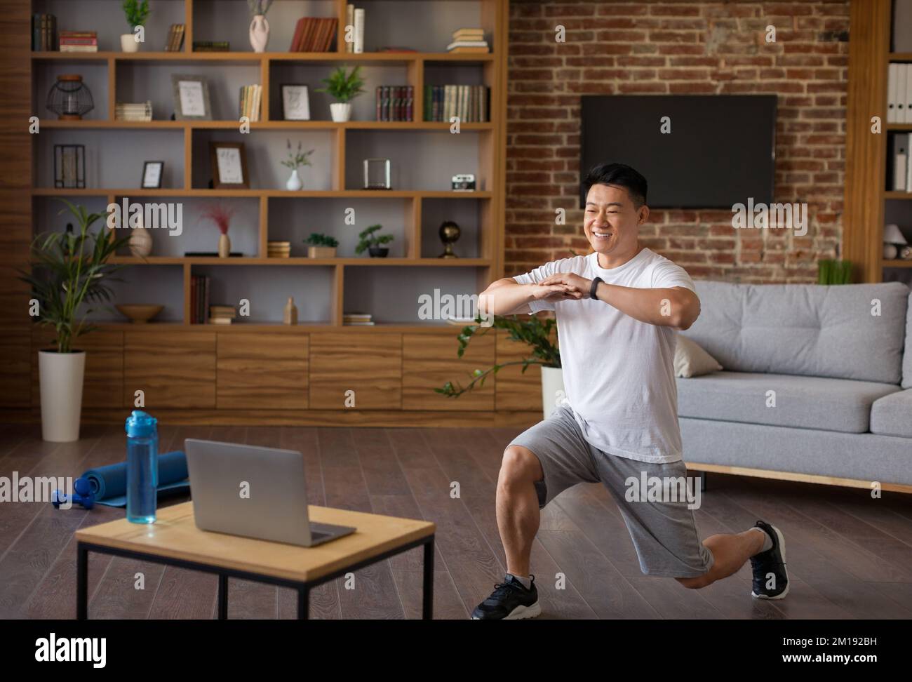 Concept de sport et de mode de vie sain. Homme asiatique actif regardant un tutoriel d'entraînement sur un ordinateur portable et faisant des fentes avant Banque D'Images
