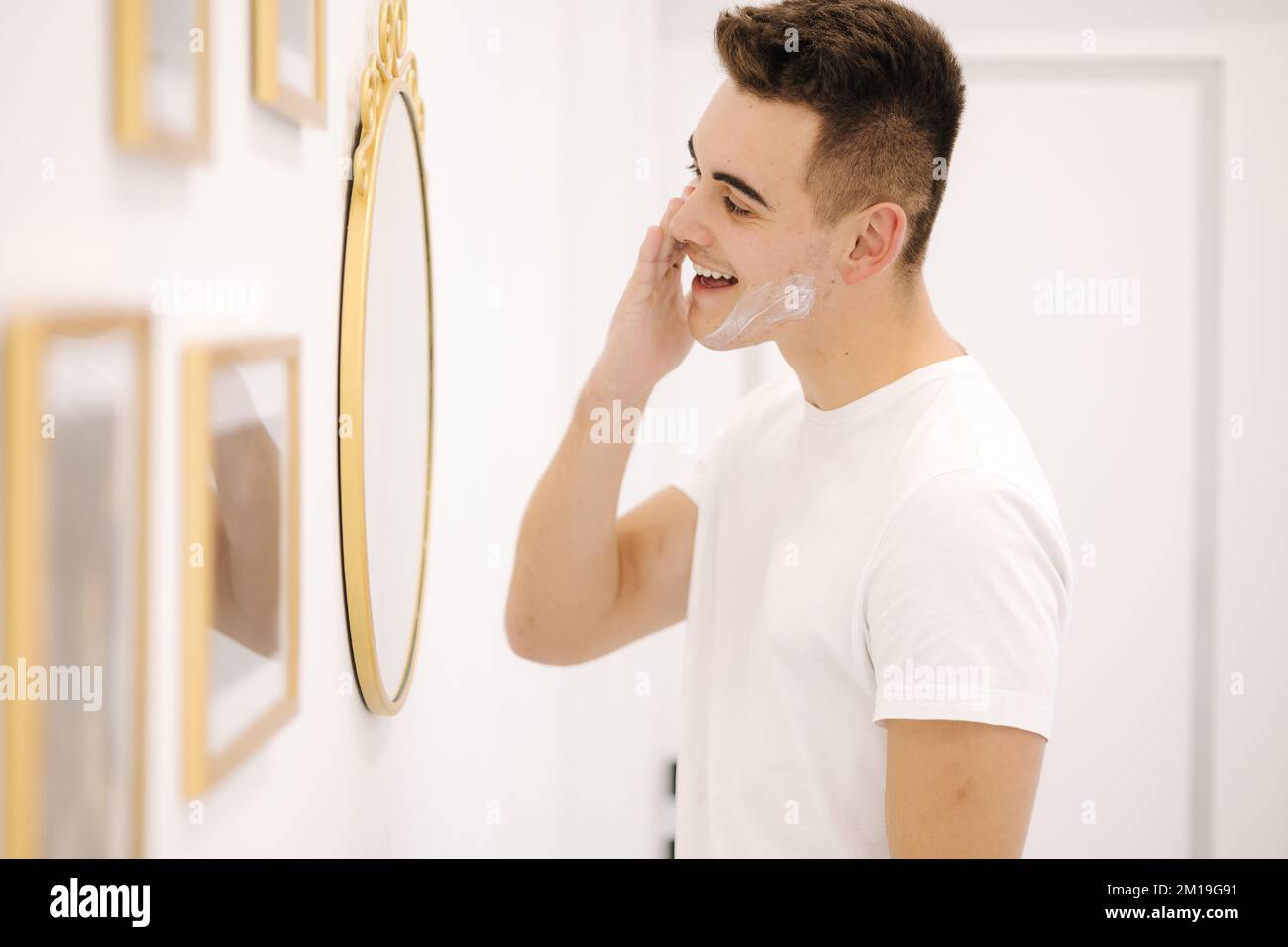 Un homme souriant applique de la crème sur le visage. Homme debout avec miroir dans un studio de beauté Banque D'Images