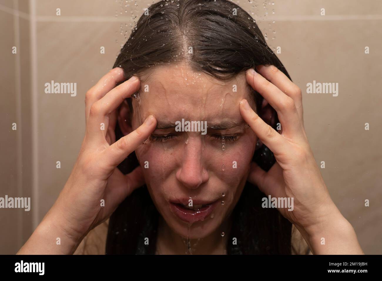 Jeune femme sous la douche avec de l'eau qui coule le long de son visage, tenant sa tête. Concept: Tenir sa tête, se sentir déprimé, se sentir en bas, burnout Banque D'Images