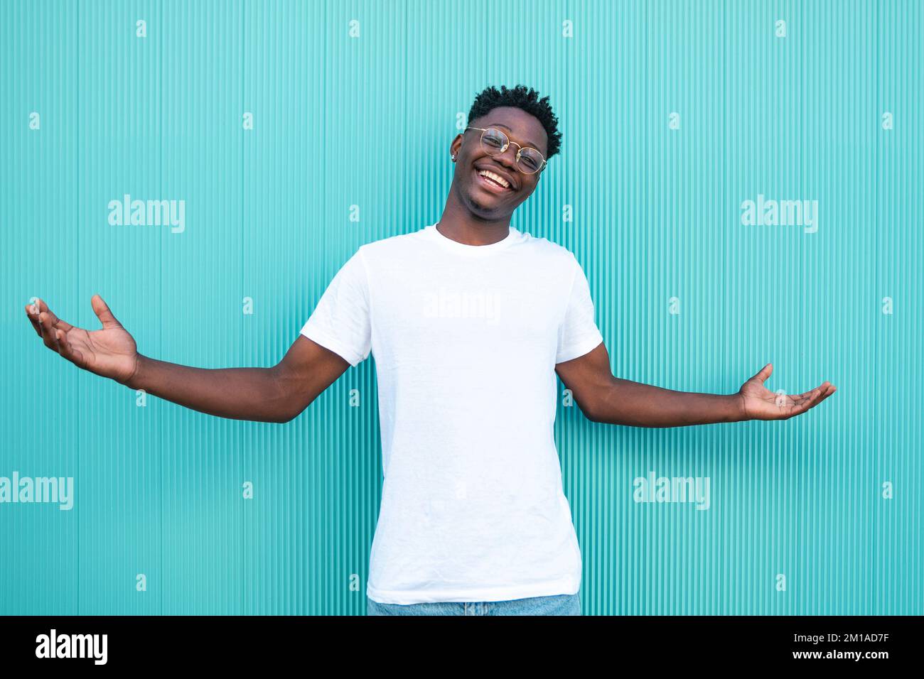 Portrait d'un homme afro-américain souriant avec ses bras ouverts sur fond turquoise et t-shirt blanc. Banque D'Images