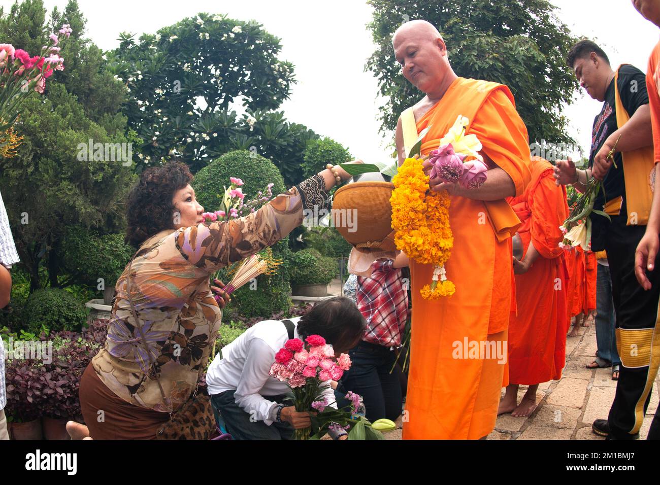 Groupe de moines recevant une offrande de fleurs de personnes à Tak Bat