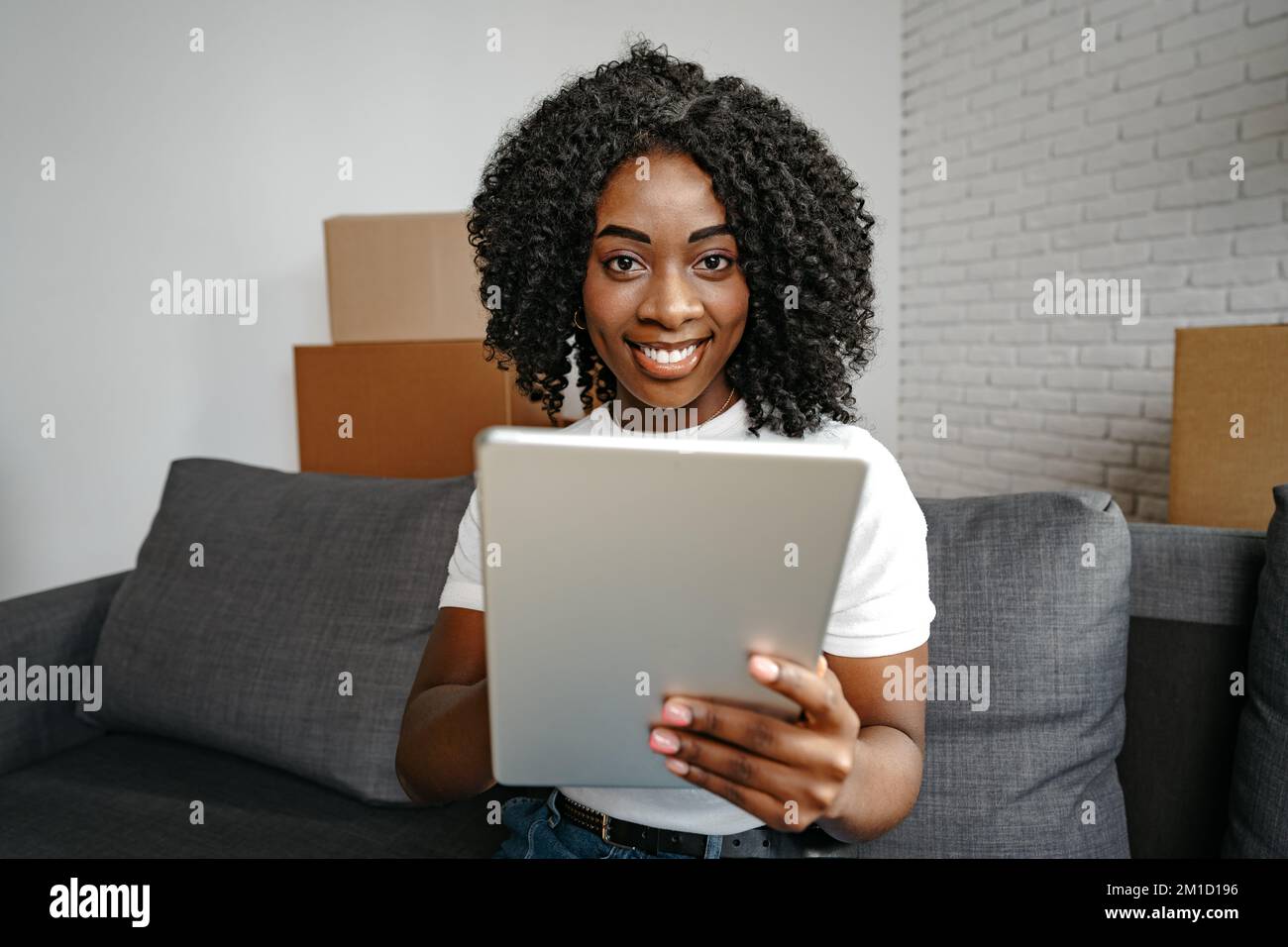 Jeune femme africaine utilisant une tablette numérique et souriant tout en se reposant à la maison. Banque D'Images