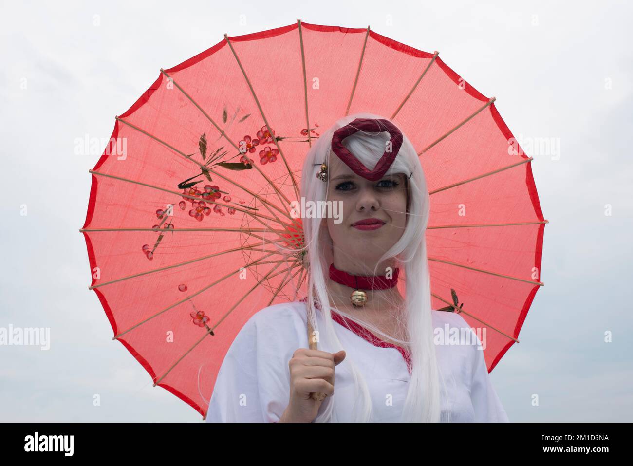 Un participant au festival Animique, vêtu d'un costume blanc et d'un parapluie rouge Banque D'Images
