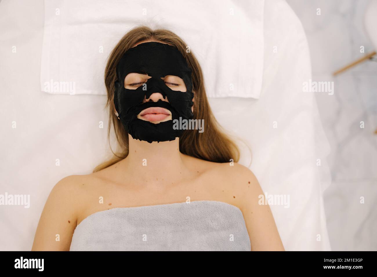 Femme avec un masque noir hydratant en tissu sur son visage en studio de beauté. Soins du visage et soins de beauté Banque D'Images