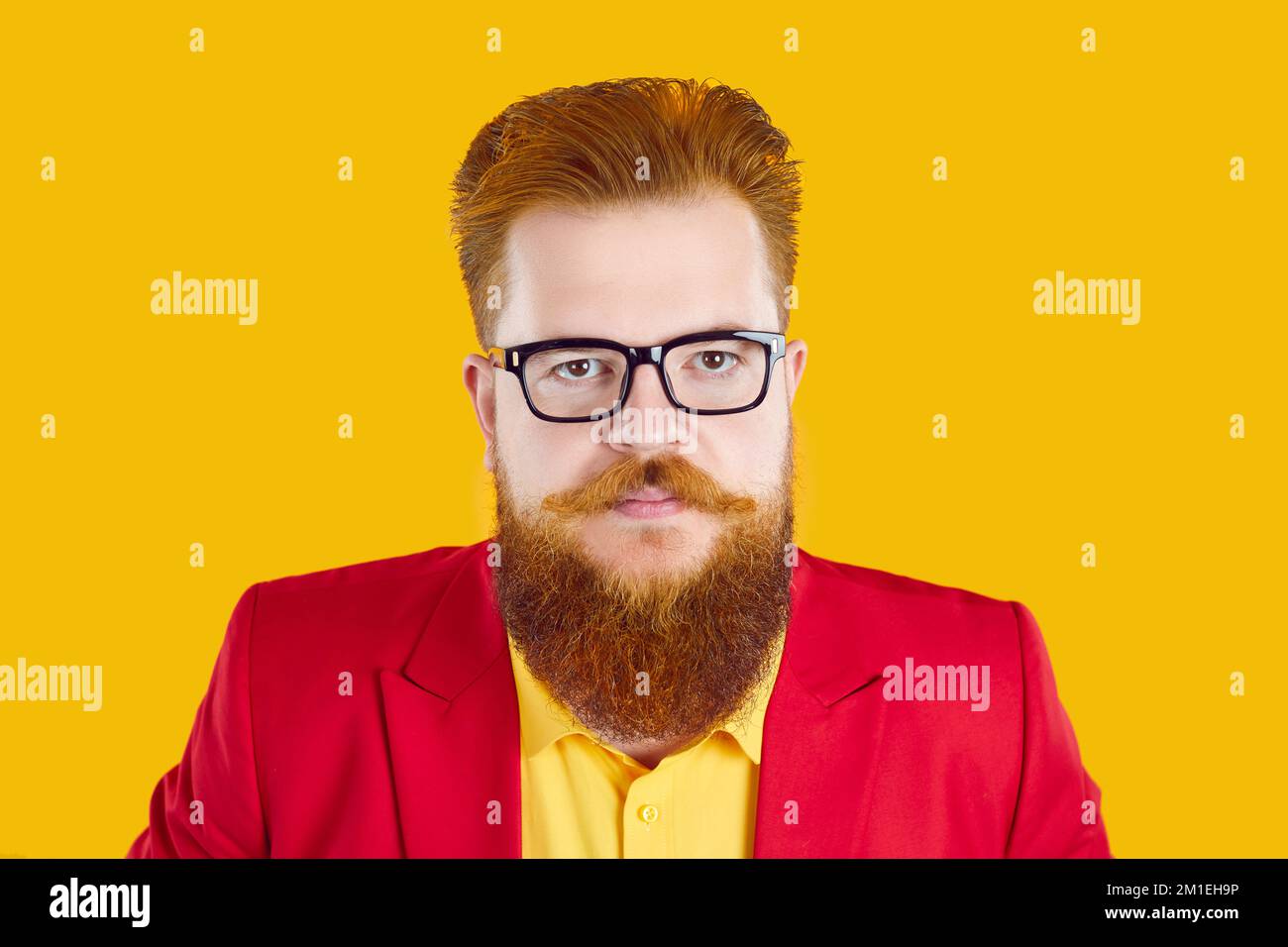 Homme barbu portant une veste rouge et des lunettes regardant un appareil photo avec une expression sérieuse du visage Banque D'Images