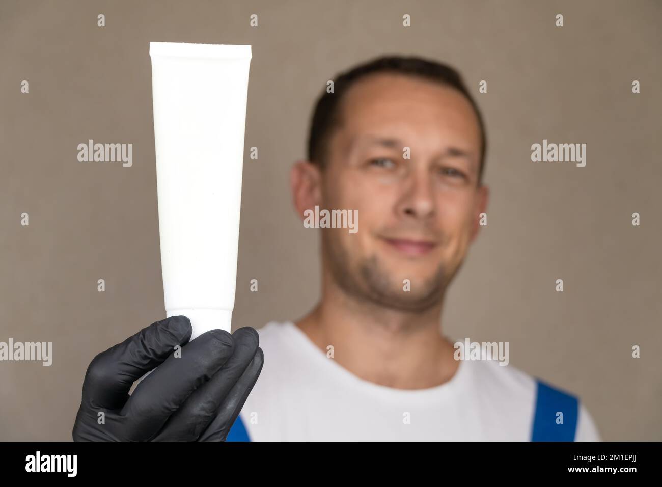 L'employé en uniforme bleu et T-shirt blanc tient le tube blanc sur lequel vous pouvez placer le logo ou le texte. Espace pour la copie. Banque D'Images