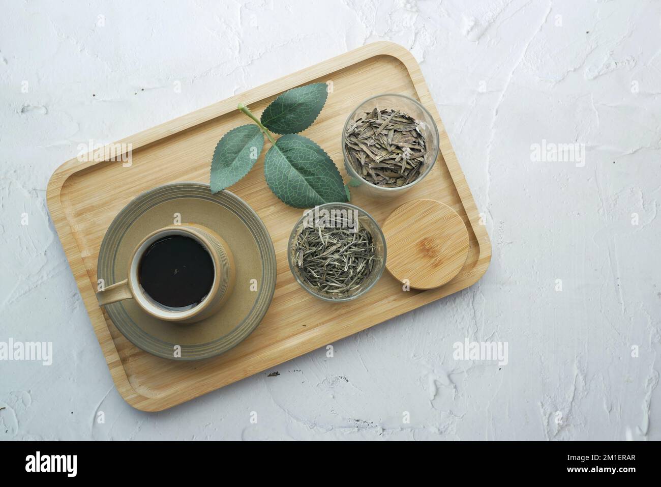 feuilles de thé séchées dans un récipient et une tasse de thé sur une table Banque D'Images