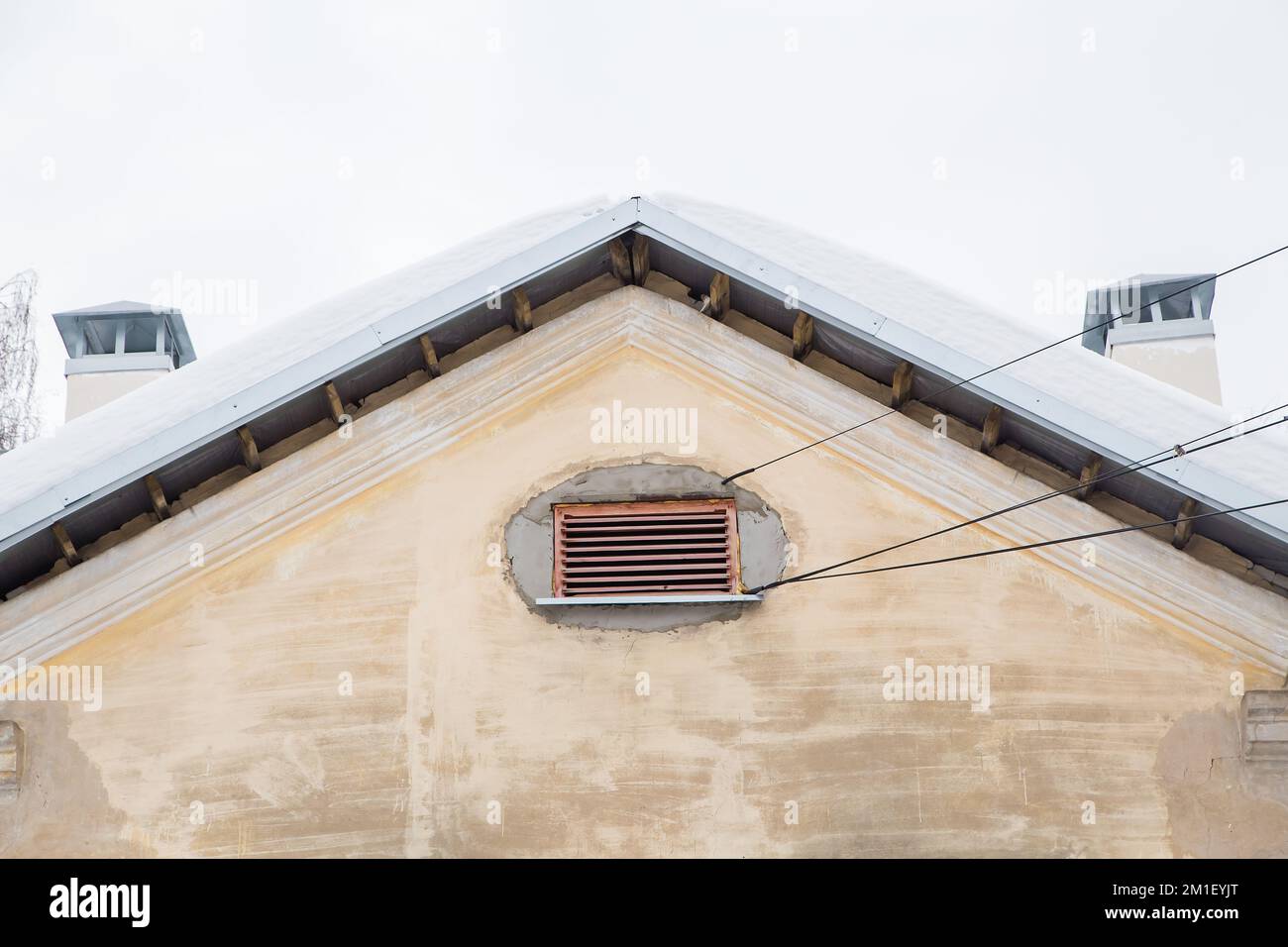 Deux tuyaux d'échappement de fumée, rectangulaires, sur le toit d'une ancienne maison. Le toit du bâtiment est recouvert de neige blanche contre le ciel gris. Nuageux, froid jour d'hiver, lumière douce. Banque D'Images