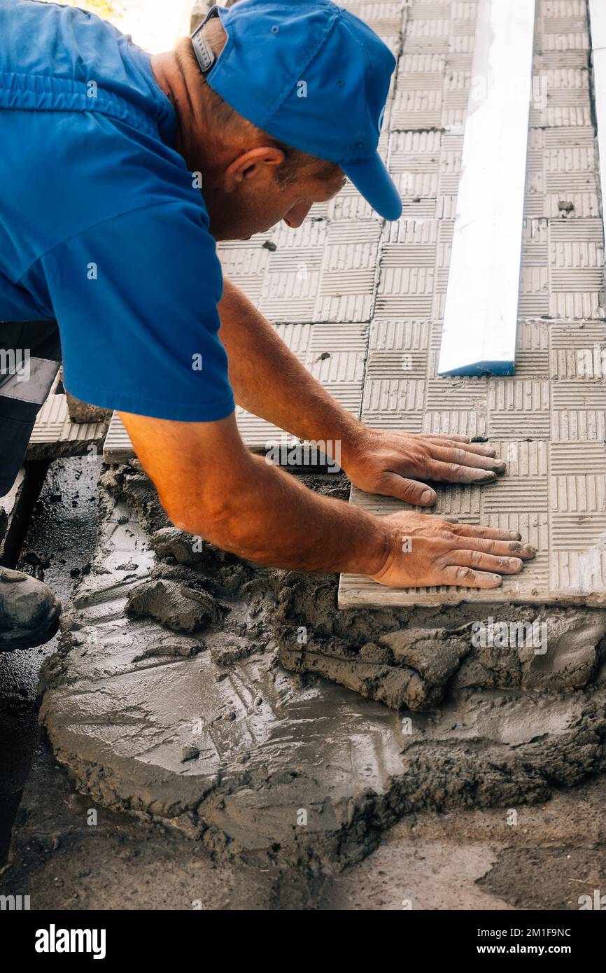 Le calque de briques pose des carreaux. Un constructeur professionnel en combinaison et casquette de baseball au travail. Maçon âgé travaillant à l'extérieur. Gros plan... Banque D'Images