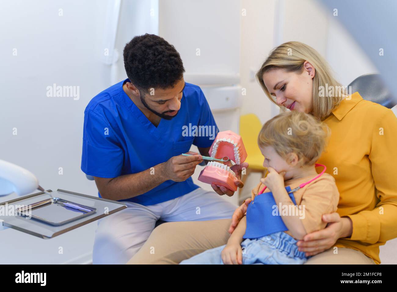 Jeune dentiste multiracial montrant une petite fille comment nettoyer les dents. Banque D'Images