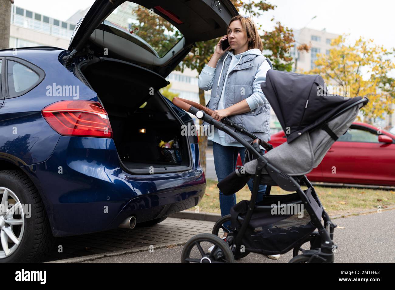 une mère adulte avec une poussette de bébé dans le coffre ouvert d'une  voiture parle au téléphone Photo Stock - Alamy