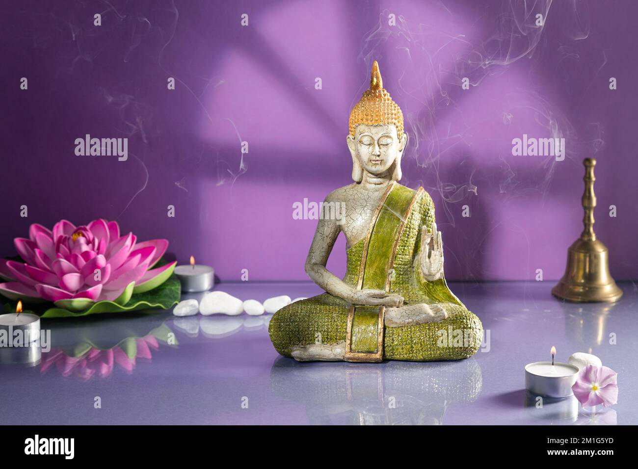 Statue de bouddha verte et dorée en méditation sur fond violet clair avec espace de copie. Banque D'Images