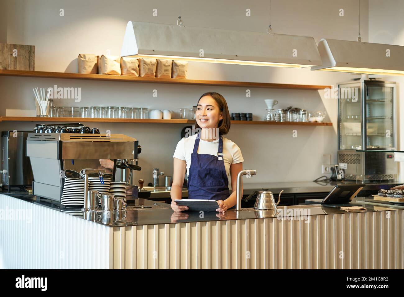 Café-restaurant. Le barista coréen souriant, une femme travaillant derrière  le comptoir, utilisant une tablette pour prendre les commandes au café,  porte un tablier bleu au travail Photo Stock - Alamy