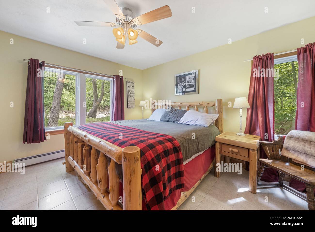 Vue intérieure d'une chambre avec ventilateur de plafond, lit en rondins et murs jaune clair. Banque D'Images