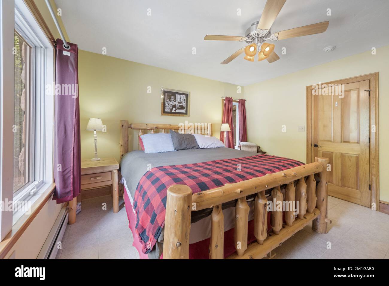 Vue intérieure d'une chambre avec ventilateur de plafond, lit en rondins et murs jaune clair. Banque D'Images