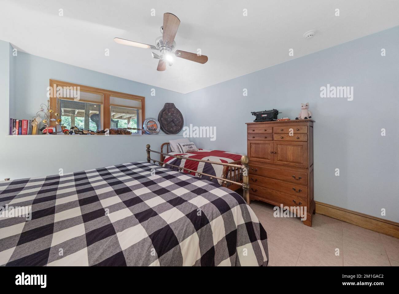 Vue intérieure d'une chambre avec ventilateur de plafond, commode en bois et murs bleu clair. Banque D'Images