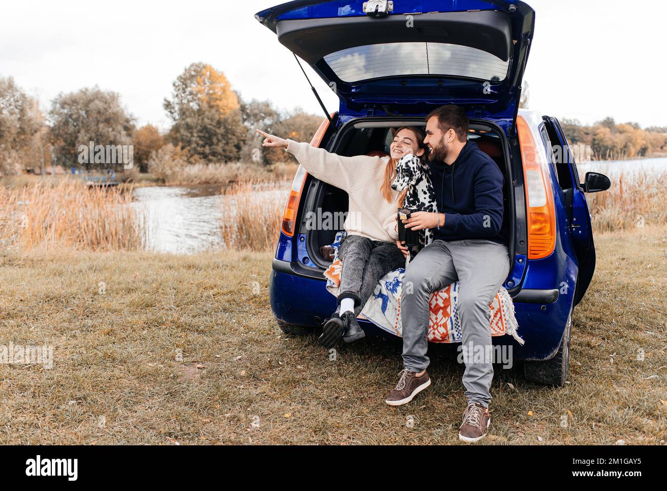 Un homme avec une femme s'amuse avec son chien en plein air dans la forêt près de la voiture. Banque D'Images