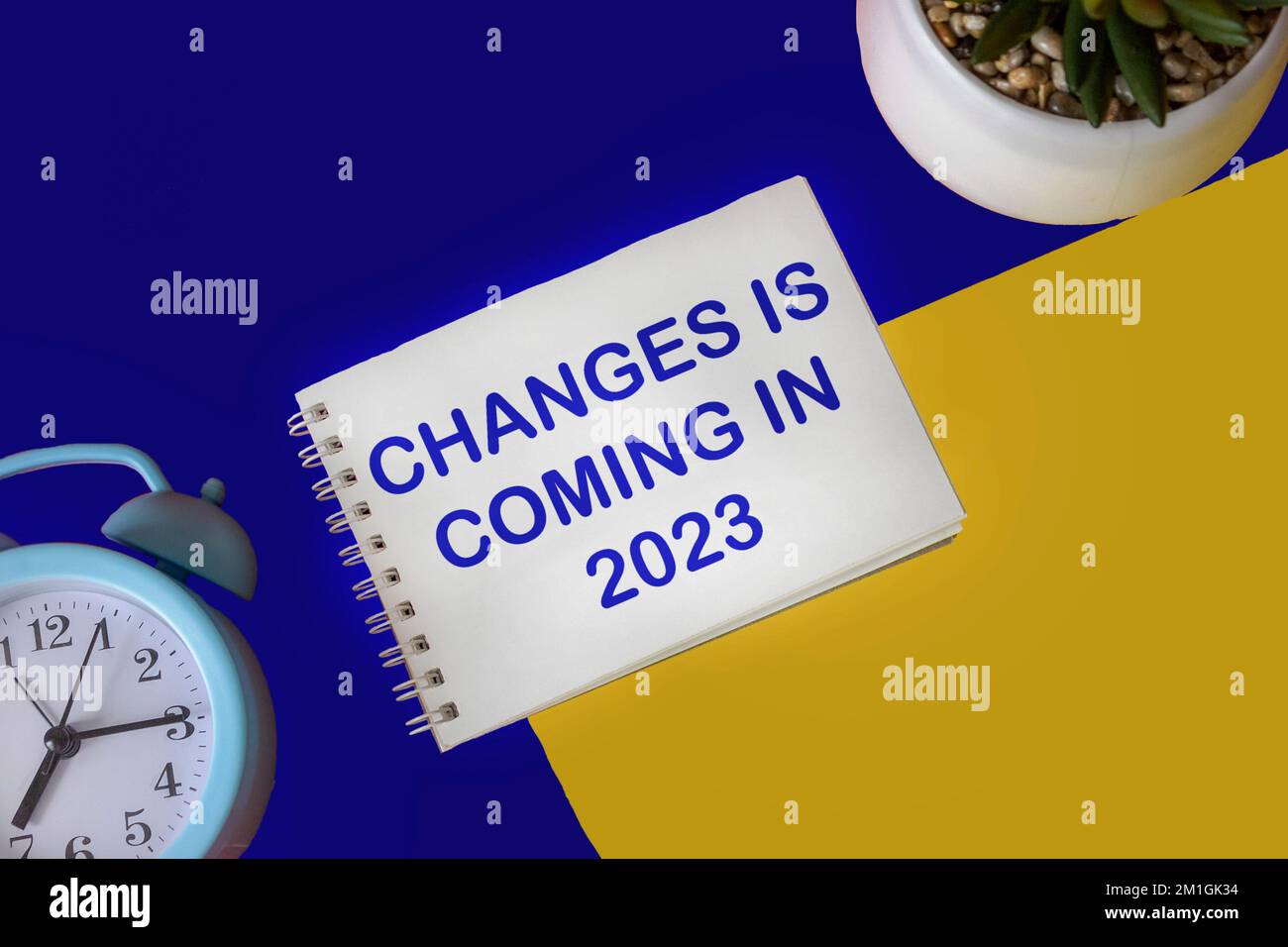 Bloc-notes avec modifications de texte dans 2023 sur fond jaune et bleu avec horloge et fleur de cactus Banque D'Images