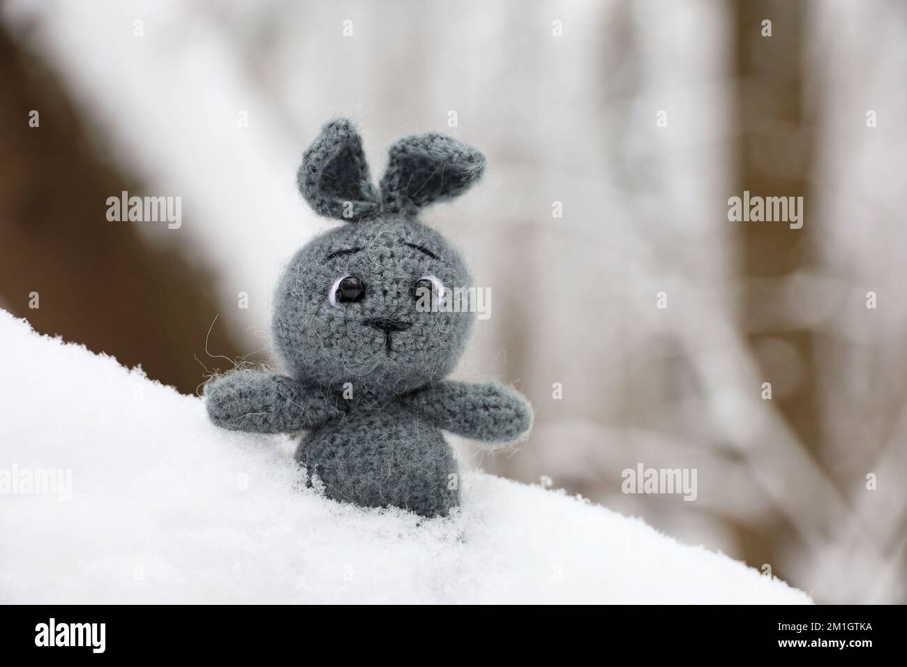 Lapin tricoté gris sur une branche d'arbre recouvert de neige. Symbole du nouvel an chinois 2023 Banque D'Images